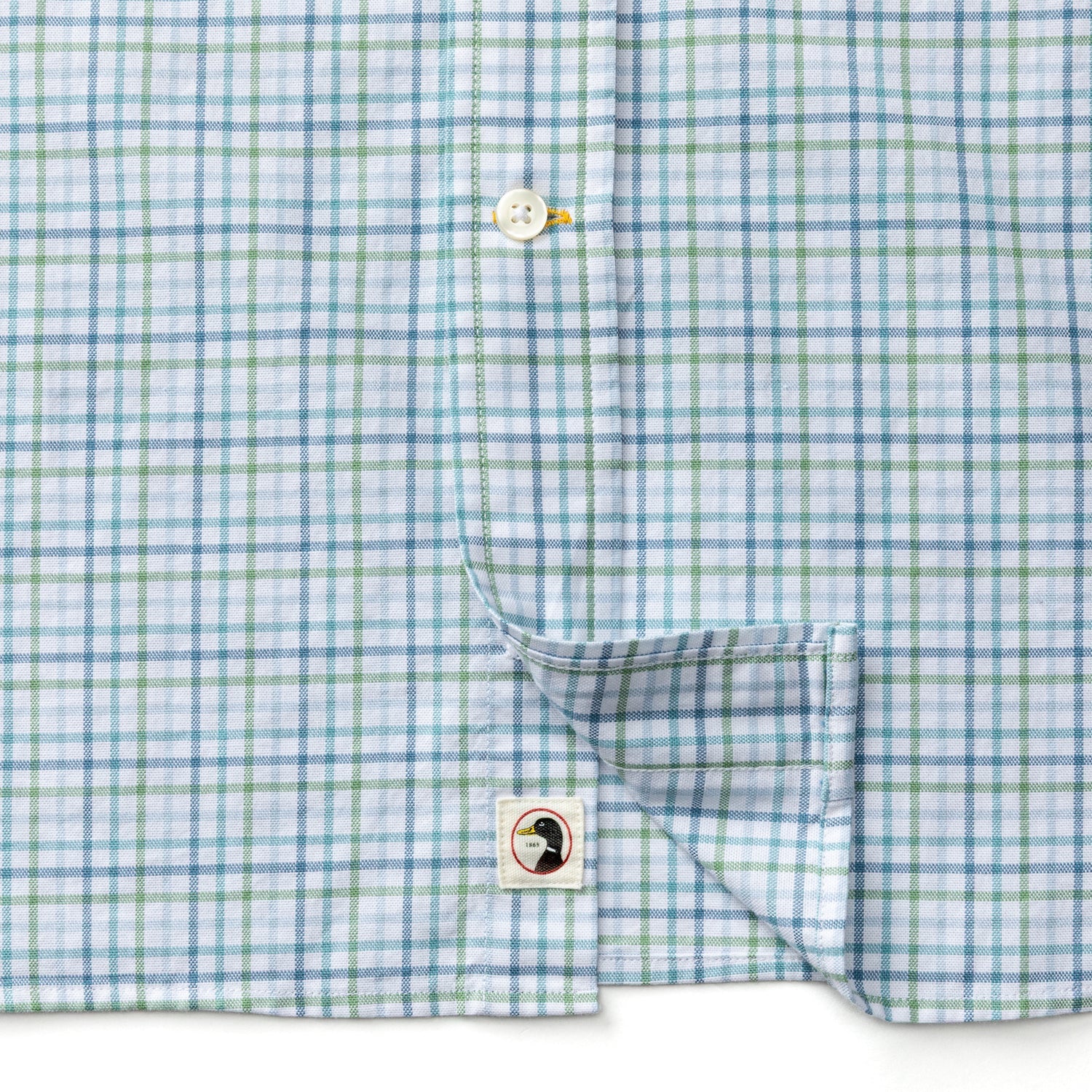 The Cotton Oxford Sport Shirt by Duck Head features light blue, white, and green plaid, a button placket, and a small bird logo patch near the hem, inspired by classic Duck Head OCBD style.