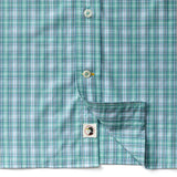 Close-up of the Duck Head Performance Poplin Sport Shirt in green and blue plaid, with one side lifted to reveal a small tag displaying the black and white Duck Head logo.