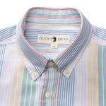 A close-up of the Duck Head Cotton Oxford Sport Shirt, featuring vertical pastel stripes in blue, pink, yellow, and green with mechanical stretch and a "Duck Head" label on the collar.
