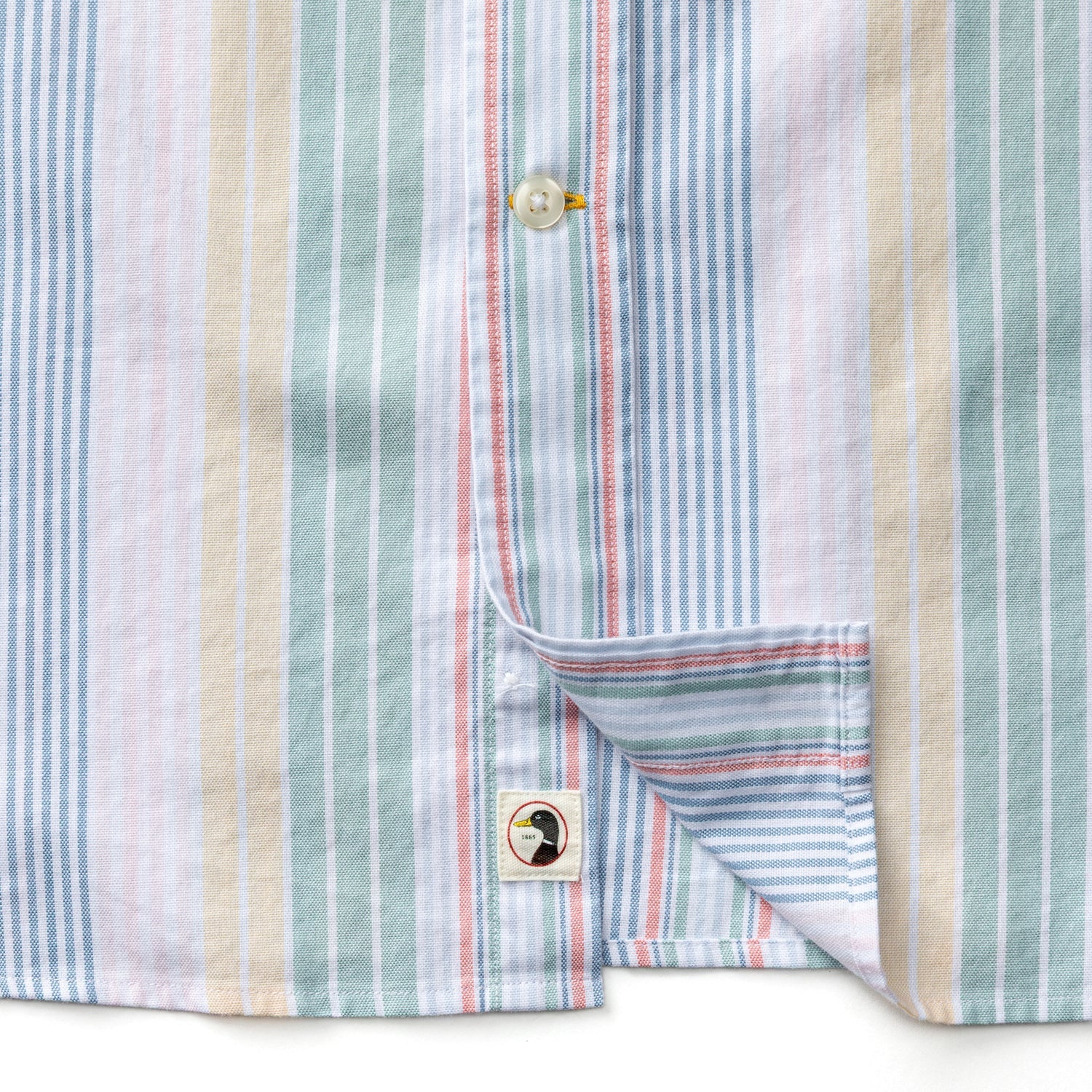 Close-up of the Duck Head Cotton Oxford Sport Shirt featuring vertical pastel blue, pink, green, and beige stripes, pearl buttons, mechanical stretch fabric, and a small square label near the hem.