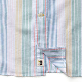 Close-up of the Duck Head Cotton Oxford Sport Shirt featuring vertical pastel blue, pink, green, and beige stripes, pearl buttons, mechanical stretch fabric, and a small square label near the hem.