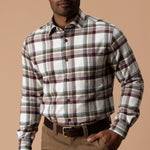 A man wears a Huckleberry Cotton Flannel Sport Shirt by Duck Head in white, maroon, and blue plaid, tucked into brown trousers with a brown leather belt.