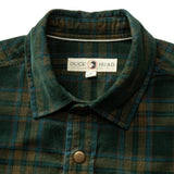 Close-up of a green and blue plaid Duck Head Corduroy Snap Shirt featuring a collar, a metal snap button, and a brand label at the neckline.