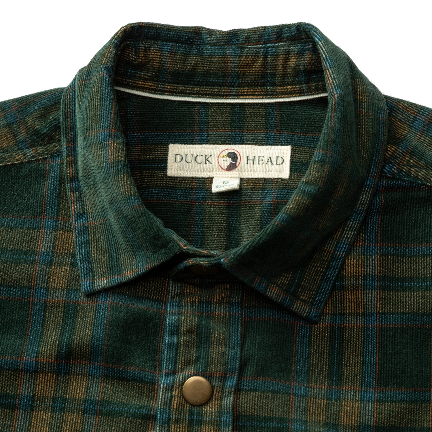 Close-up of a green and blue plaid Duck Head Corduroy Snap Shirt featuring a collar, a metal snap button, and a brand label at the neckline.