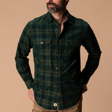 A man wears a Duck Head Corduroy Snap Shirt in a dark green and navy plaid cotton corduroy with two chest pockets.