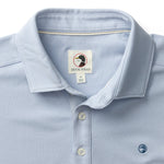 The Duck Head Hanover Pima Cotton Pique Polo features a light blue hue, classic collar, button placket, small chest logo embroidery, and a branded label inside the collar.