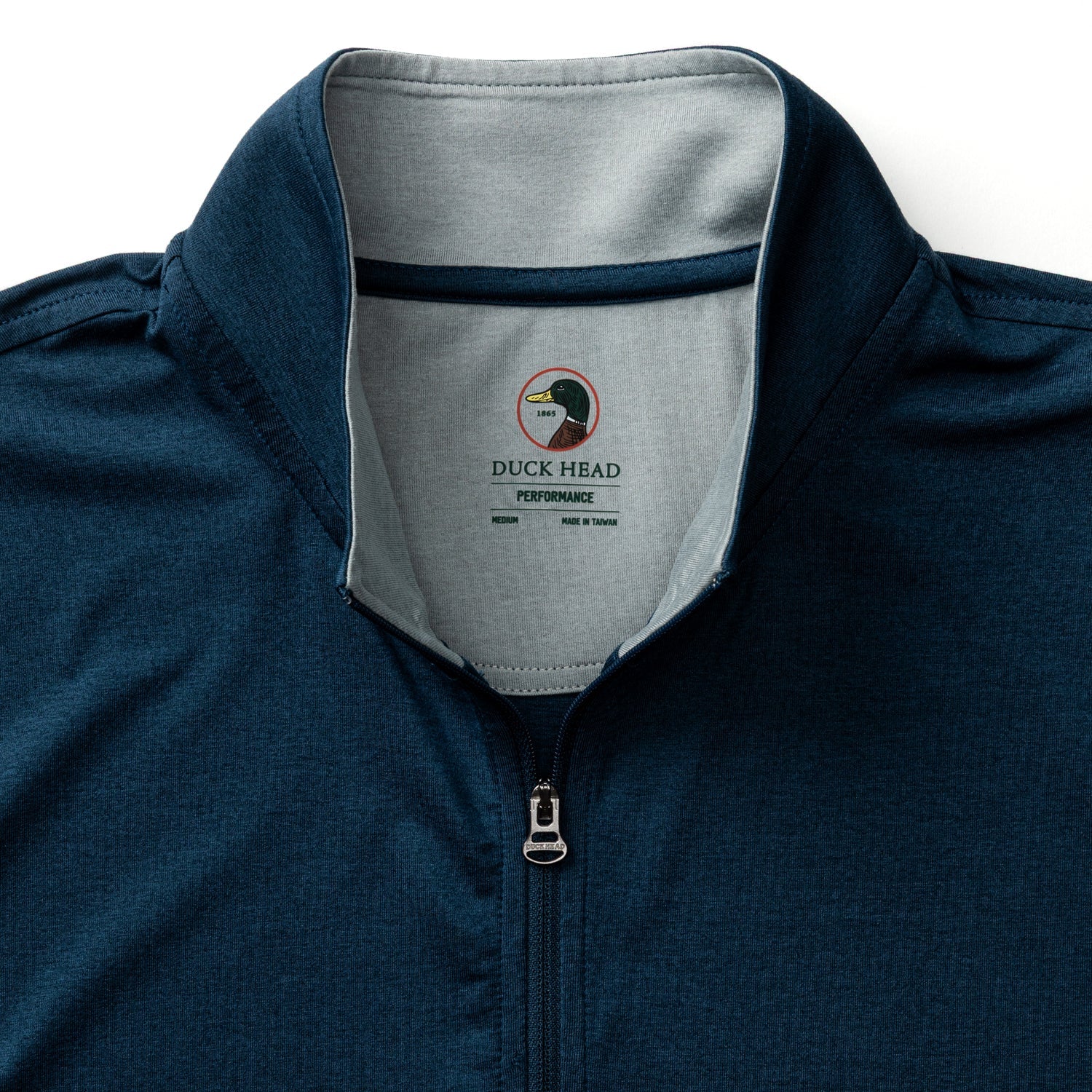 The Duck Head Long Drive Performance 1/4 Zip Pullover is navy blue with a light gray inner collar, made from moisture-wicking fabric and features a “Duck Head Performance” label inside the neckline.