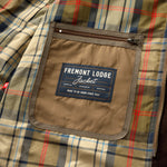Interior view of a Duck Head Fremont Lodge Performance Quilted Jacket with a plaid lining and a zippered pocket featuring a label that reads “Fremont Lodge Jacket, made to be worn since 1865.”.