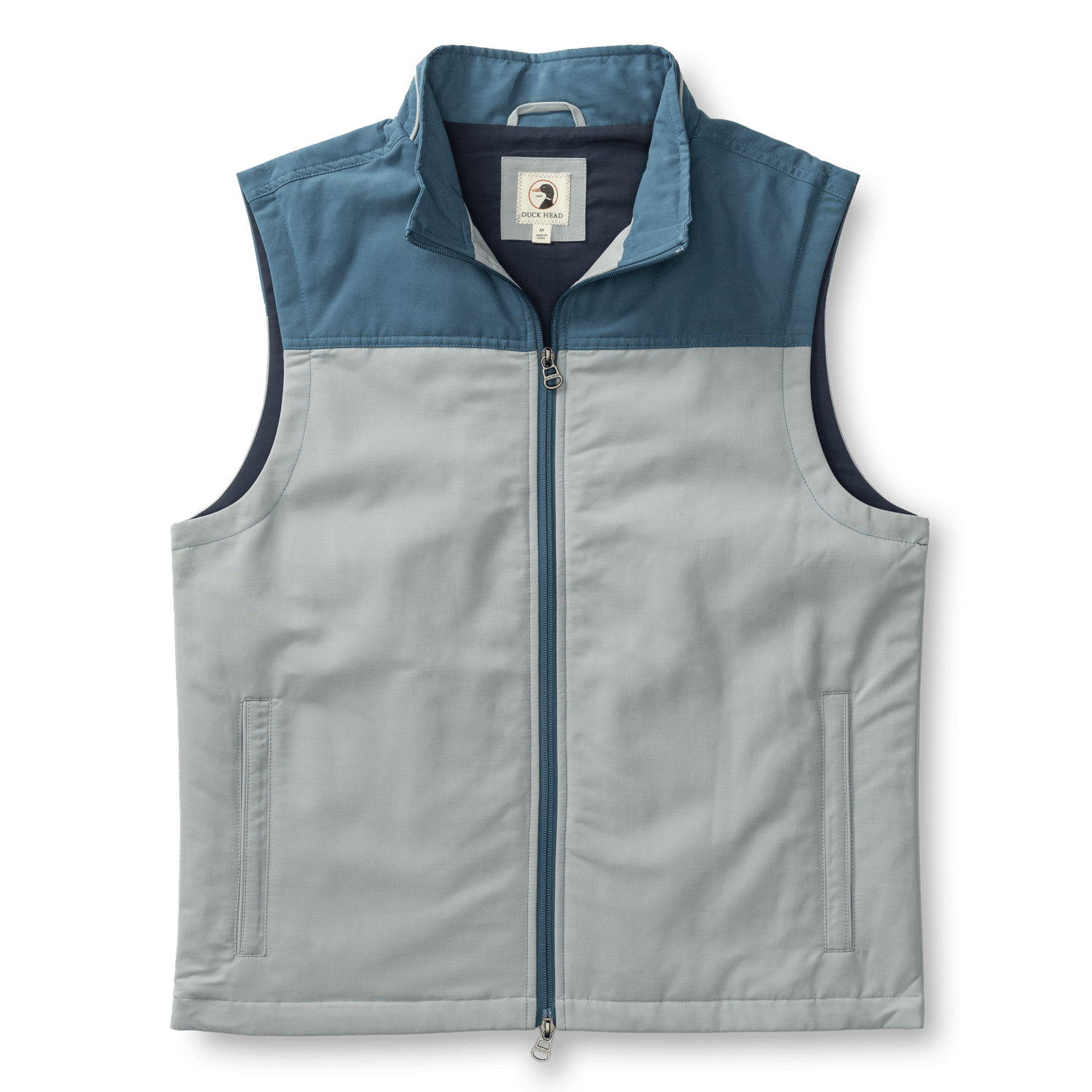 The Duck Head Long Drive Performance vest is sleeveless and zip-up, with a high collar, light gray body, dark blue shoulder yoke, water-repellent fabric, and two side pockets.