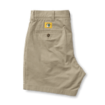 A pair of folded Duck Head 7in Gold School men’s chino shorts with a buttoned back pocket and a yellow globe logo patch above the pocket.