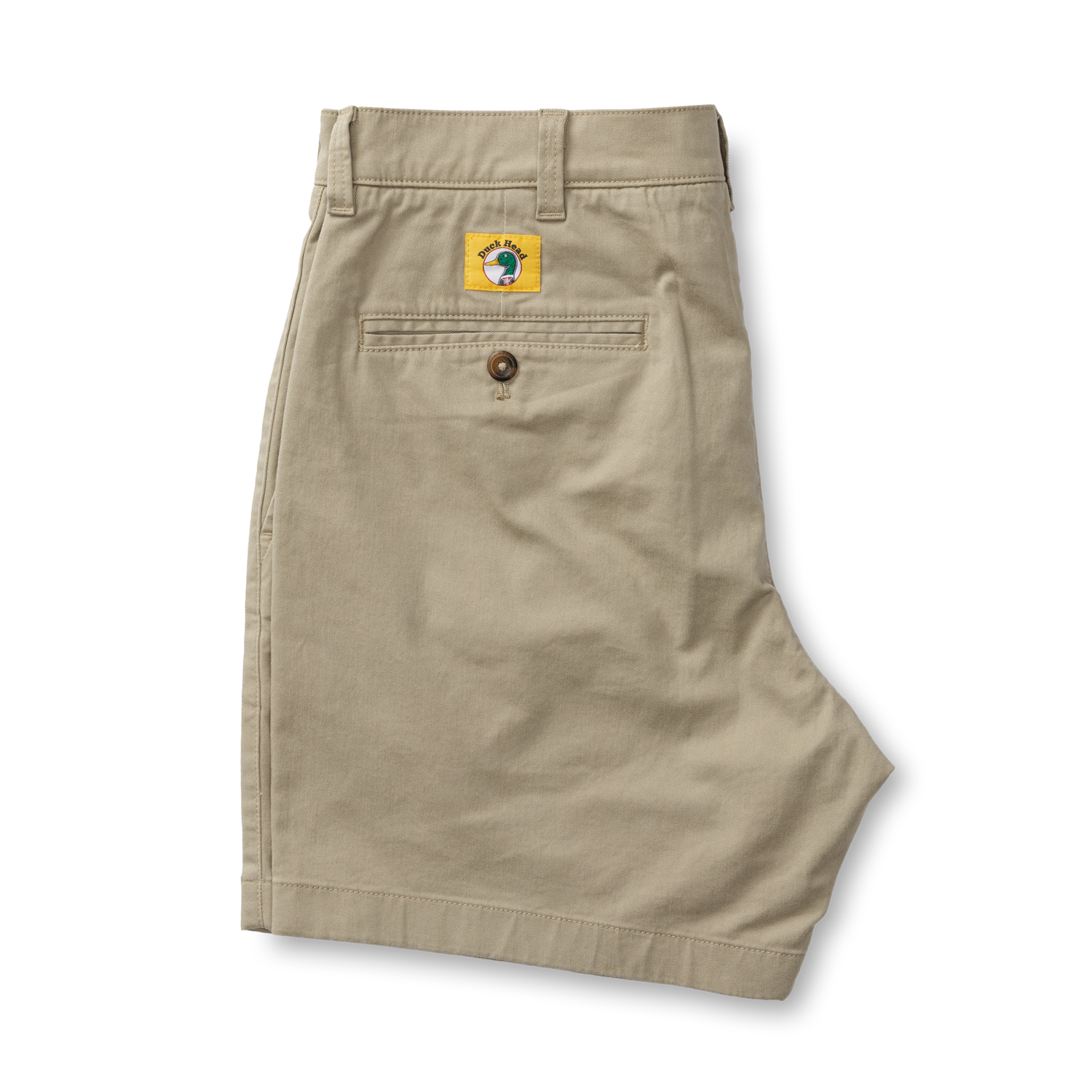 A pair of folded Duck Head 7in Gold School men’s chino shorts with a buttoned back pocket and a yellow globe logo patch above the pocket.