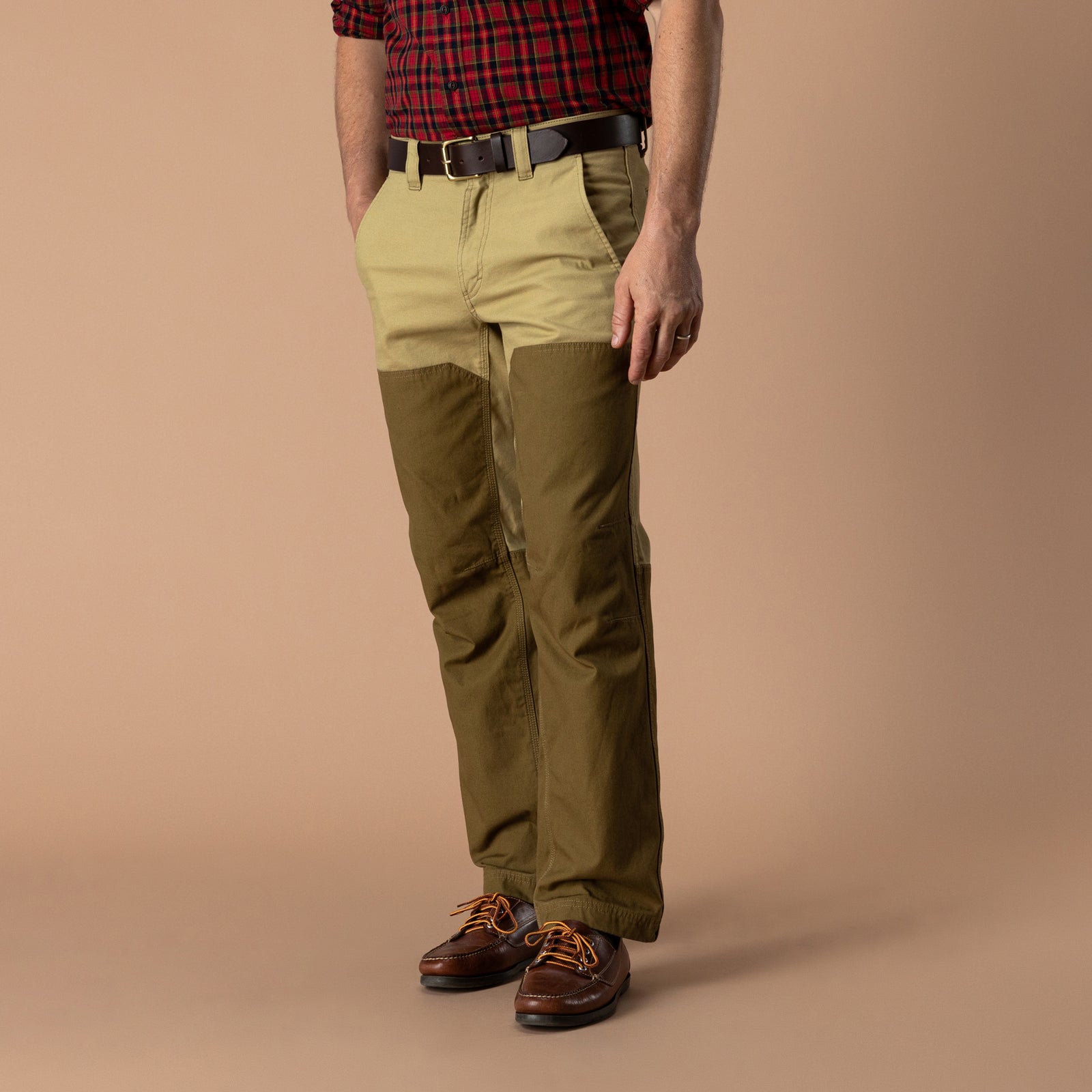 A person wearing a red plaid shirt, a brown belt, leather shoes, and Duck Head Field Canvas Briar Pant in two-tone khaki and olive green.