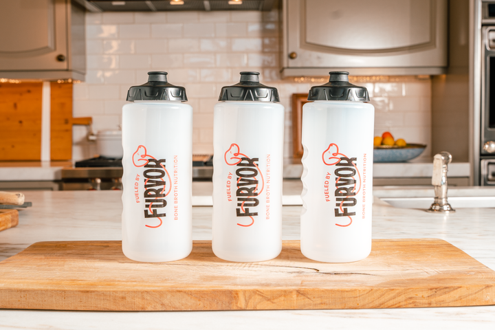 Three Furvor Squeeze Bottles For Dogs, BPA-free with black lids labeled "Fueled by FURJOY," are lined up on a wooden cutting board—perfect for serving Furvor bone broth to your pets.