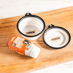 A bottle of Furvor bone broth for dogs sits beside a Furvor Collapsible Water Bowl and a black travel pet bowl, all neatly arranged on a wooden surface.
