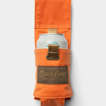 The Duck Camp Canvas Can Holster—a waxed orange canvas can holder featuring a brown “Duck Camp” patch—secures a canned beverage, shown against a plain white background.
