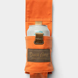 The Duck Camp Canvas Can Holster—a waxed orange canvas can holder featuring a brown “Duck Camp” patch—secures a canned beverage, shown against a plain white background.