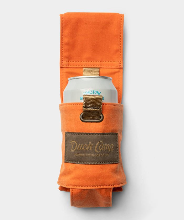 The Duck Camp Canvas Can Holster—a waxed orange canvas can holder featuring a brown “Duck Camp” patch—secures a canned beverage, shown against a plain white background.