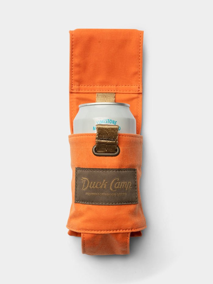 The Duck Camp Canvas Can Holster—a waxed orange canvas can holder featuring a brown “Duck Camp” patch—secures a canned beverage, shown against a plain white background.