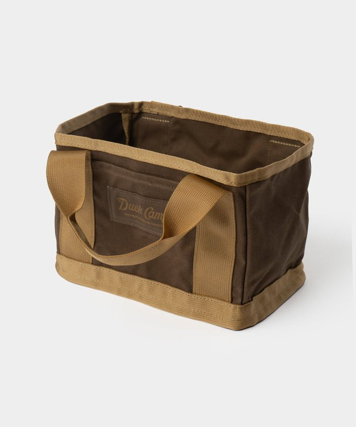 The Duck Camp Canvas Ammo Tote by Duck Camp is a rectangular brown and tan canvas bag featuring two sturdy handles and reinforced seams, shown against a plain white background.