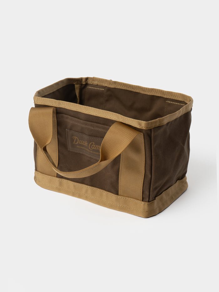 The Duck Camp Canvas Ammo Tote by Duck Camp is a rectangular brown and tan canvas bag featuring two sturdy handles and reinforced seams, shown against a plain white background.