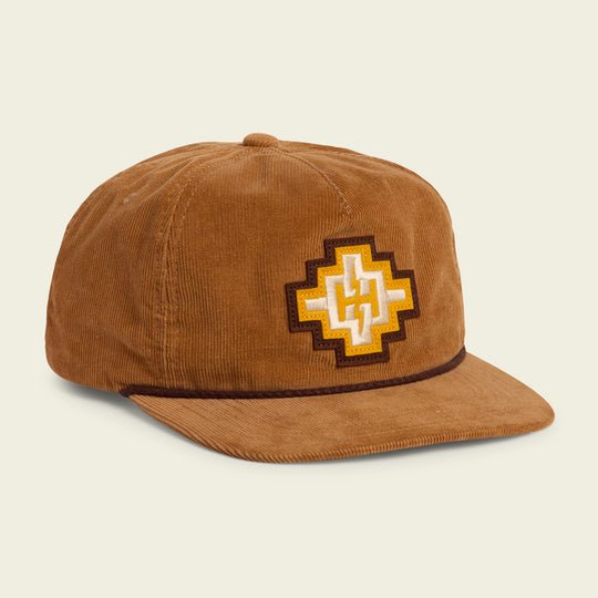 Howler Brothers Bolt Motif corduroy baseball cap in brown, featuring a yellow and white geometric patch on the front and a dark brown trim along the brim, shown on a light background.