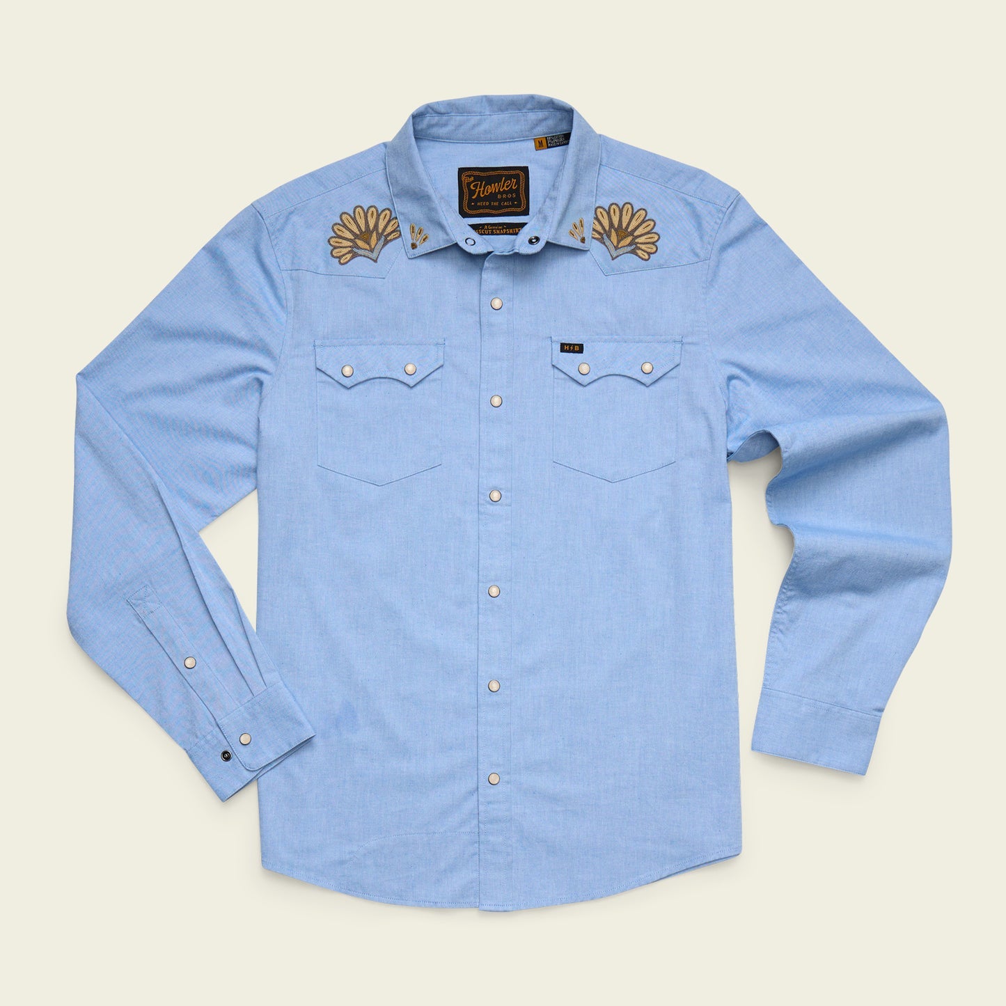 Howler Brothers Crosscut Deluxe Longsleeve in light blue, reminiscent of a faded blue oxford, features Fanned Flora embroidery on the collar, two chest pockets, and classic pearl snap buttons.