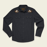 The Howler Brothers Crosscut Deluxe is a black, long-sleeve button-up shirt crafted from soft stretch chambray. It features two chest pockets, classic western yokes for a timeless look, and embroidered white and brown flower designs on the shoulders, all inspired by the rugged style of Howler Brothers.