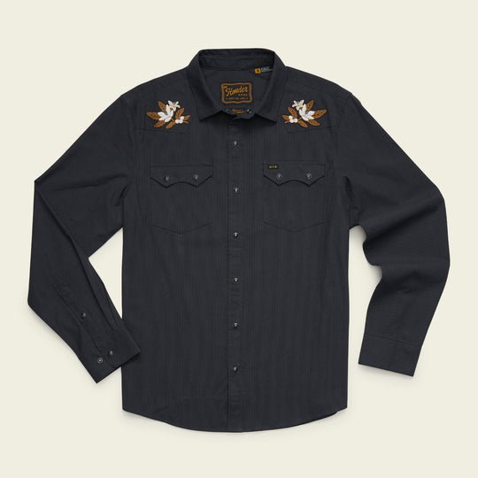 The Howler Brothers Crosscut Deluxe is a black, long-sleeve button-up shirt crafted from soft stretch chambray. It features two chest pockets, classic western yokes for a timeless look, and embroidered white and brown flower designs on the shoulders, all inspired by the rugged style of Howler Brothers.