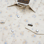 Close-up of the Howler Brothers H Bar B Snapshirt in cream, featuring a floral pattern, two front pockets with pearl snaps, and a small “H.B” tag on the right pocket flap—hallmarks of Howler Brothers’ signature style.