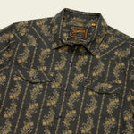 A dark button-up technical utility shirt with a yellow floral stripe pattern, featuring two chest pockets with flaps, pearl snaps for added style, and a “Howler Brothers” label on the inside collar.