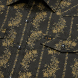 Close-up of a Howler Brothers Grampa’s Curtains black technical utility shirt featuring gold floral patterns, a buttoned front with pearl snaps, two chest pockets with flaps, and a small “H|B” tag above the left pocket.
