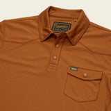 Howler Brothers Ranchero Tech is a rust-colored short-sleeve polo shirt featuring a front pocket, buttons, and a Howler Brothers label on the inside collar.