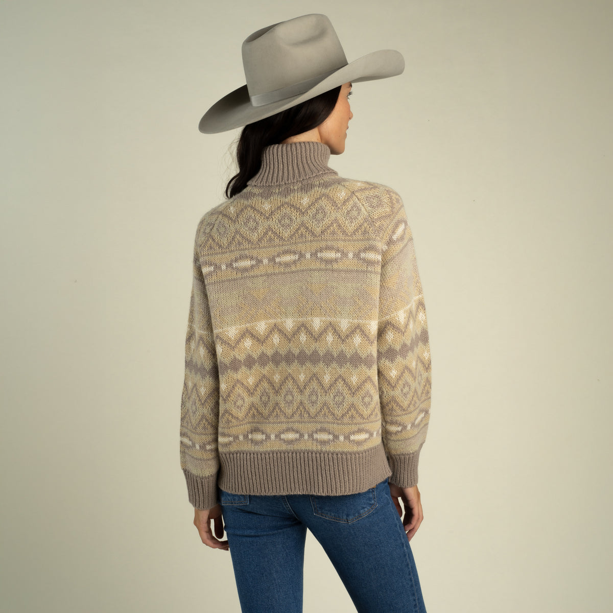 A person wearing a grey cowboy hat and a tan, brown, and cream southwest-inspired Shiloh Sweater by Sendero Provisions Co. with ribbed cuffs.