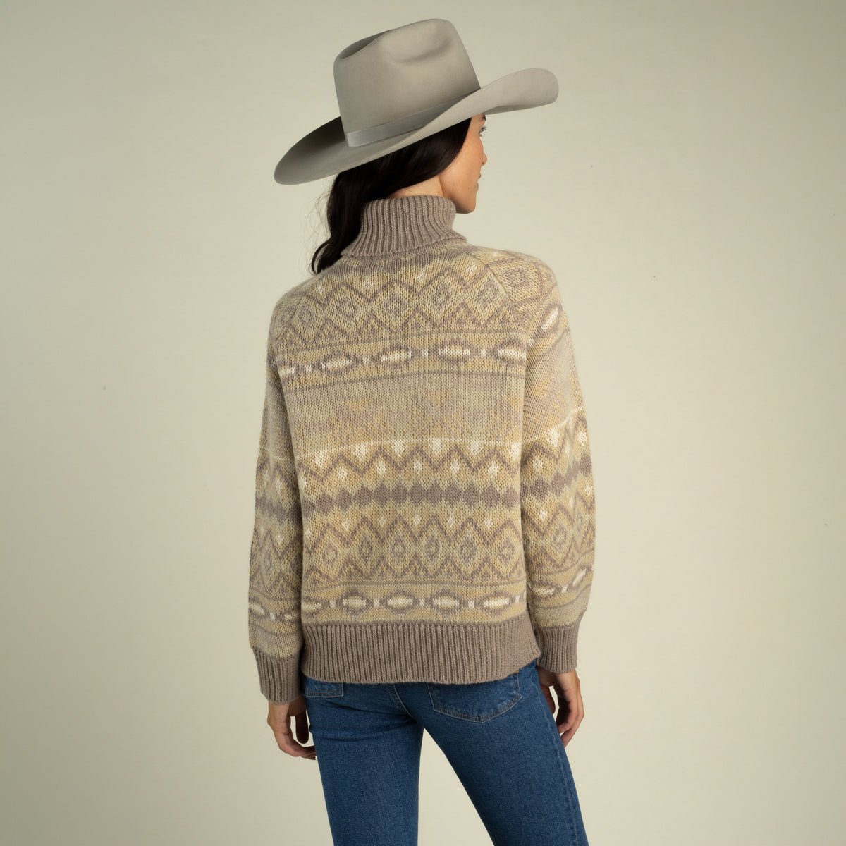 A person wearing a grey cowboy hat and a tan, brown, and cream southwest-inspired Shiloh Sweater by Sendero Provisions Co. with ribbed cuffs.