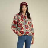 A woman wears a Sedona Fleece by Sendero Provisions Co. in a red and grey southwest print, paired with blue jeans and a burgundy baseball cap.