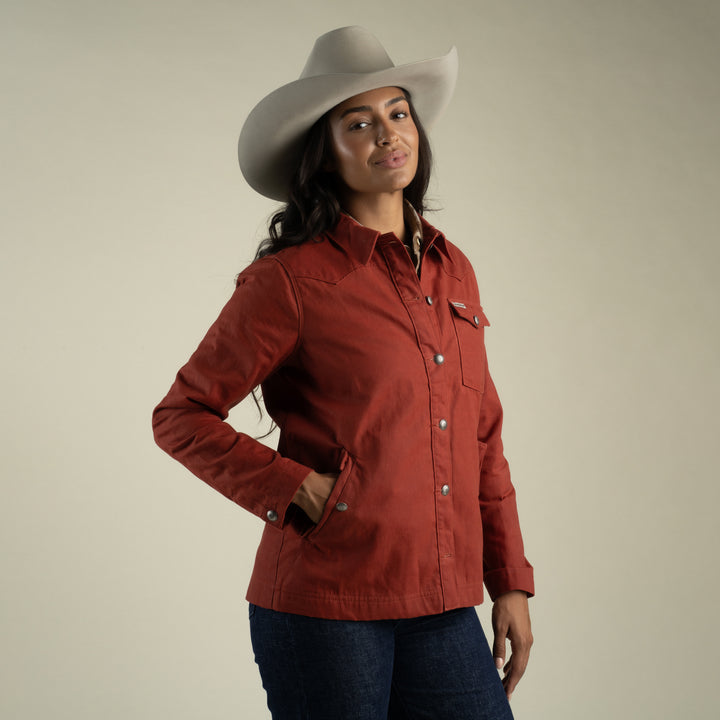 A woman wearing the Sendero Provisions Co. Women’s Rancho Waxed Jacket stands against a plain beige background.