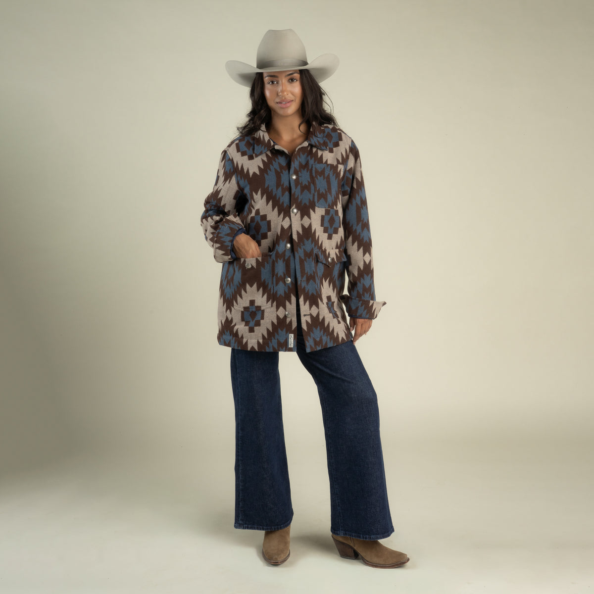 A person wearing a grey cowboy hat, a brown and blue Santa Fe Jacket by Sendero Provisions Co., dark wash wide-leg jeans, and brown boots.