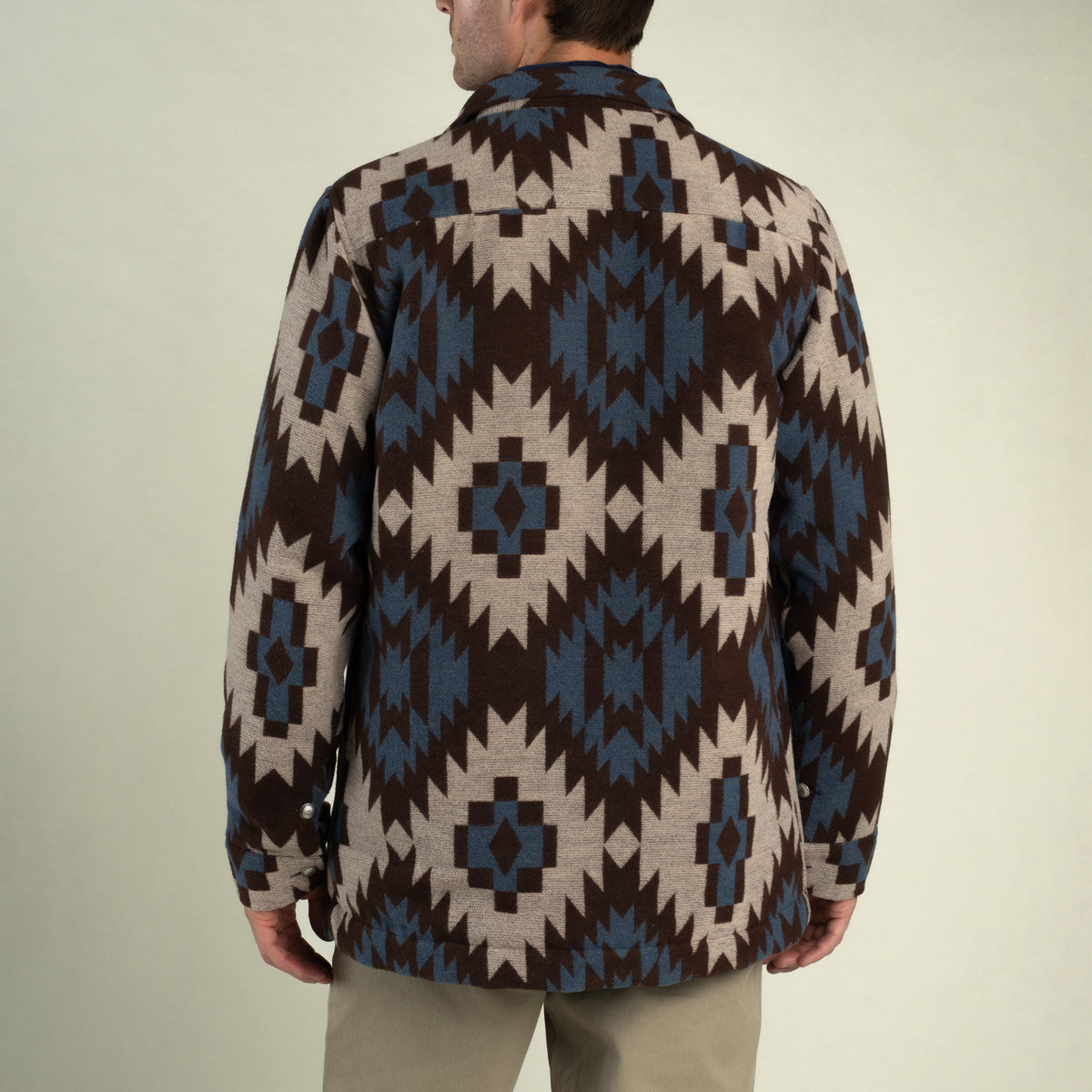 Back view of a person wearing a Santa Fe Jacket featuring a brown, tan, and blue geometric southwestern print with a button-up front.