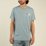 A man wearing a light blue Sendero Provisions Co. Shootin’ Hand t-shirt, crafted from ultra soft cotton with a small “Steady Hand” logo and tiger graphic on the left chest in soft touch screen print, paired with light blue jeans, stands against a plain background.