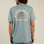 Wearing the Sendero Provisions Co. Shootin’ Hand t-shirt by Sendero Provisions Co.—a light blue, ultra-soft cotton shirt featuring a soft touch screen print graphic of skeleton hands holding a glass and the western proverb: “Never drink with your shootin’ hand.”.