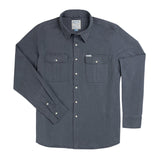 The Stamford Work Shirt Concho Blue by Sendero Provisions Co. is a long-sleeve, button-up denim shirt in a rich blue shade, featuring two front chest pockets, a collar, and classic pearl snap closures. The shirt is shown laid flat on a white background.