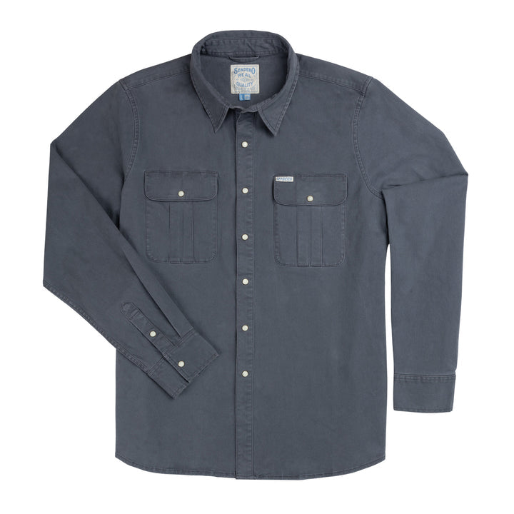 The Stamford Work Shirt Concho Blue by Sendero Provisions Co. is a long-sleeve, button-up denim shirt in a rich blue shade, featuring two front chest pockets, a collar, and classic pearl snap closures. The shirt is shown laid flat on a white background.