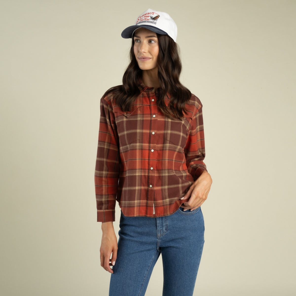 Woman wearing a cropped red and brown Sendero Women’s Durango Flannel - Pearlsnap, blue jeans, and a baseball cap.