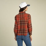 A woman seen from behind wearing a Sendero Women’s Durango Flannel - Pearlsnap in red and brown with a western-style back yoke and blue jeans.