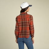 A woman seen from behind wearing a Sendero Women’s Durango Flannel - Pearlsnap in red and brown with a western-style back yoke and blue jeans.
