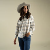 A woman wearing a tan cowboy hat and the Sendero Helena Button Down, a grey and white paisley check shirt with small floral embroidery, tucked into blue jeans.