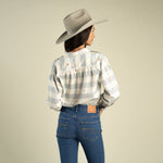 A person wearing a light grey cowboy hat, a Sendero Helena Button Down with a light blue and white paisano check and small floral embroidery, and blue jeans.