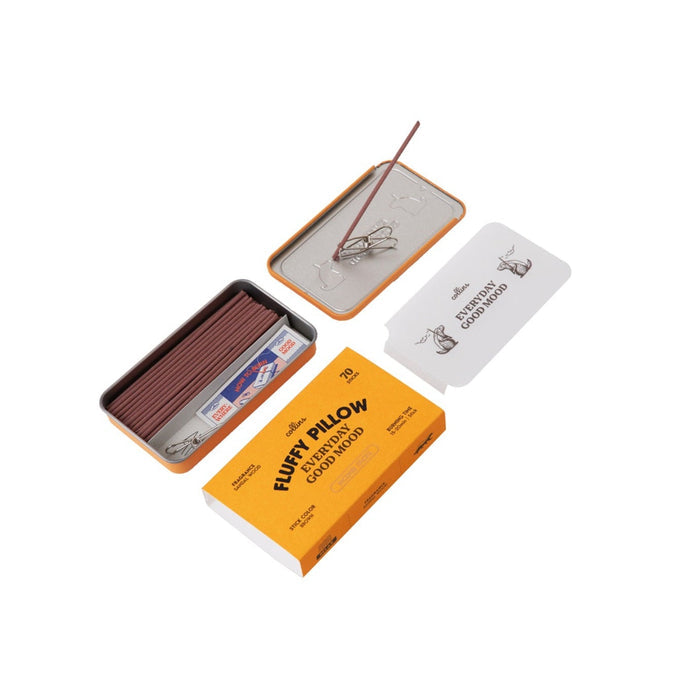 An open metal case containing Fluffy Pillow Incense Sticks by Collins, a metal holder with incense inserted, and a yellow box labeled “Fluffy Pillow Japanese Incense Good Mood” from the brand Collins.