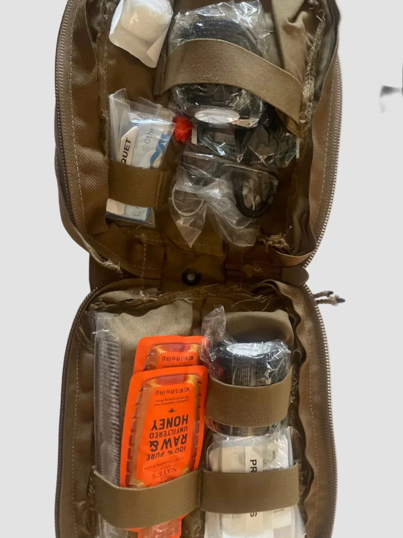 The CoveyKits Molle Kit- Working Dog First Aid Kit by CoveyKits is an open tan pouch containing essential survival and first aid supplies for pets, such as honey packets, a small comb, bandages, and various small items secured with elastic straps—perfect as a portable pet first aid kit for emergency dog care or basic wound treatment on the go.