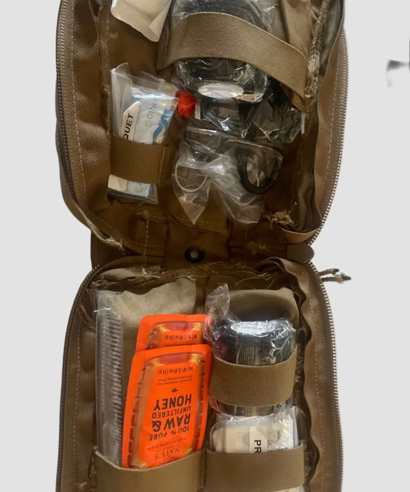 The CoveyKits Molle Kit- Working Dog First Aid Kit by CoveyKits is an open tan pouch containing essential survival and first aid supplies for pets, such as honey packets, a small comb, bandages, and various small items secured with elastic straps—perfect as a portable pet first aid kit for emergency dog care or basic wound treatment on the go.